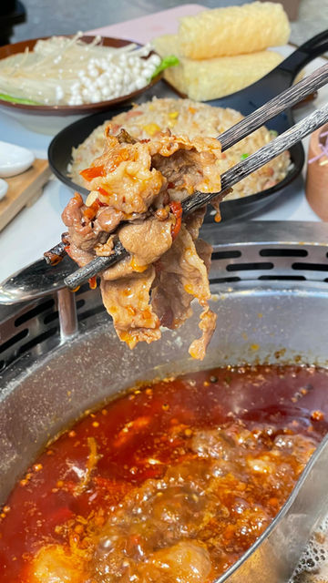 Chopsticks holding spicy cooked meat over a bubbling hot pot, with rice.