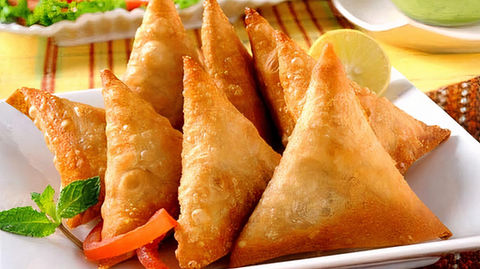 Golden-brown samosas with red bell pepper strips and lemon wedge.