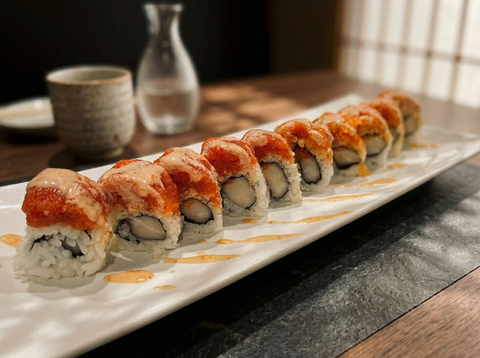 Sushi rolls with orange topping and sauce on a white plate