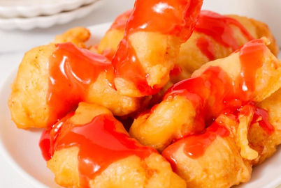 Sweet and sour chicken pieces on a white plate with red sauce drizzled.