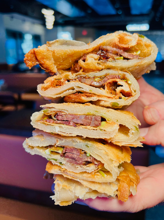 Hand holding a stack of delicious sliced flatbread with meat and vegetables.