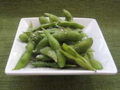 Steamed edamame sprinkled with salt, a delicious appetizer on white plate.