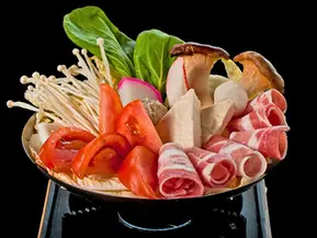 Assorted hot pot ingredients including pork, vegetables, mushrooms, tofu on a burner.