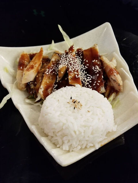 盘子里的烤鸡肉配米饭,淋上酱汁,撒上芝麻,美味可口。