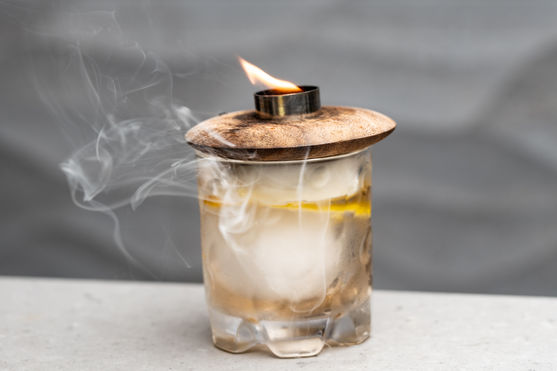 冒烟的鸡尾酒在玻璃杯中，木盖上有火焰