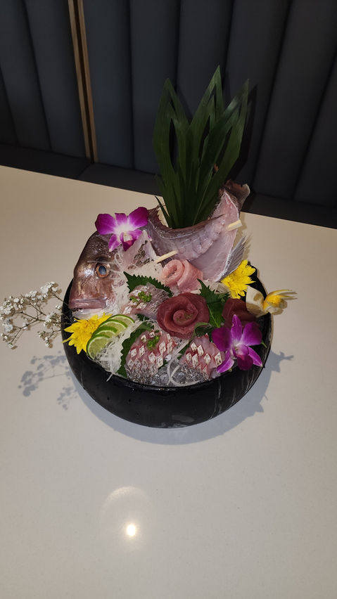 Sushi platter with fish pieces, flowers and greenery in a black bowl.