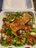 烤鲑鱼沙拉配有黄瓜、番茄和橄榄，放在白色外卖盒里。