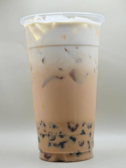 Layered bubble tea with tapioca pearls, ice, and creamy foam topping.