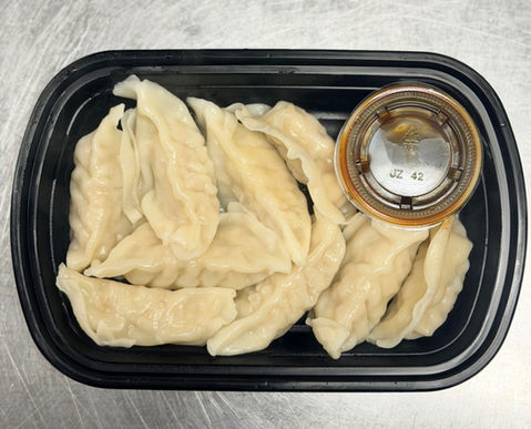 Dumplings in a black container with sauce 