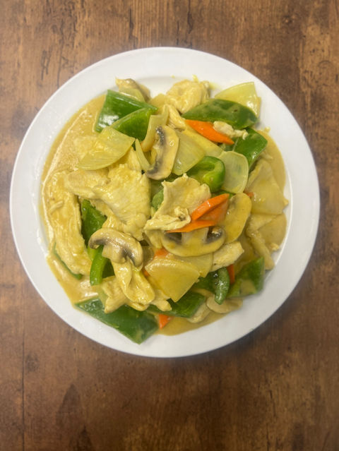 Yellow curry dish with vegetables on a white plate on wood table.
