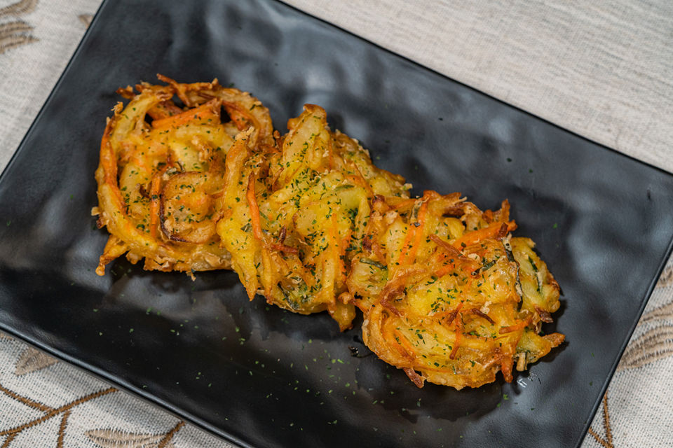 Three crispy golden vegetable fritters on a long black plate.