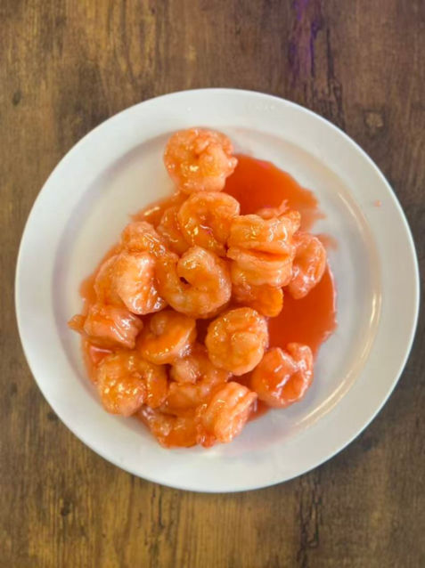 Sweet and sour shrimp on white plate, served on a wooden table.