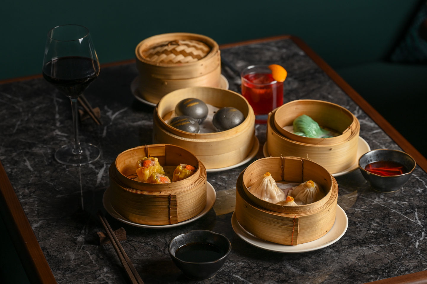 Colorful steamed dim sum dumplings in bamboo baskets with wine and cocktail.