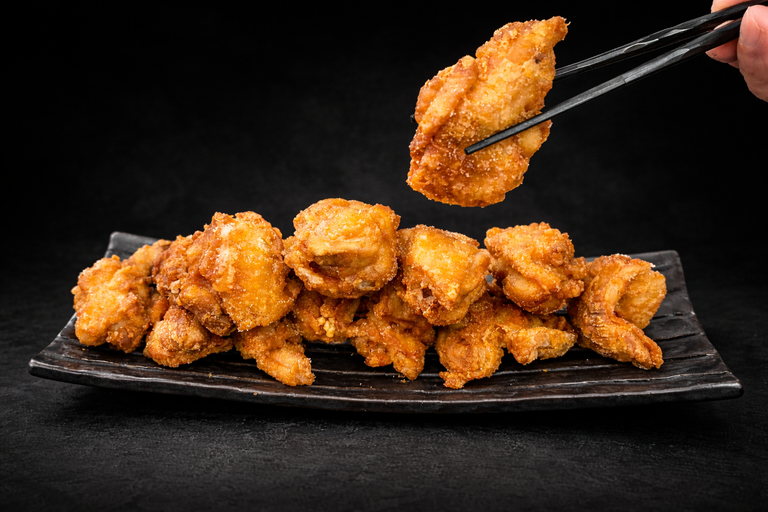 Crispy fried chicken pieces on a black plate, being held by chopsticks.