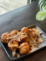 Takoyaki balls served with toppings on a plate near a plant.