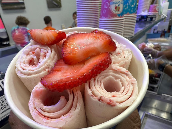 Fresh strawberry rolled ice cream in bowl with sliced strawberries.