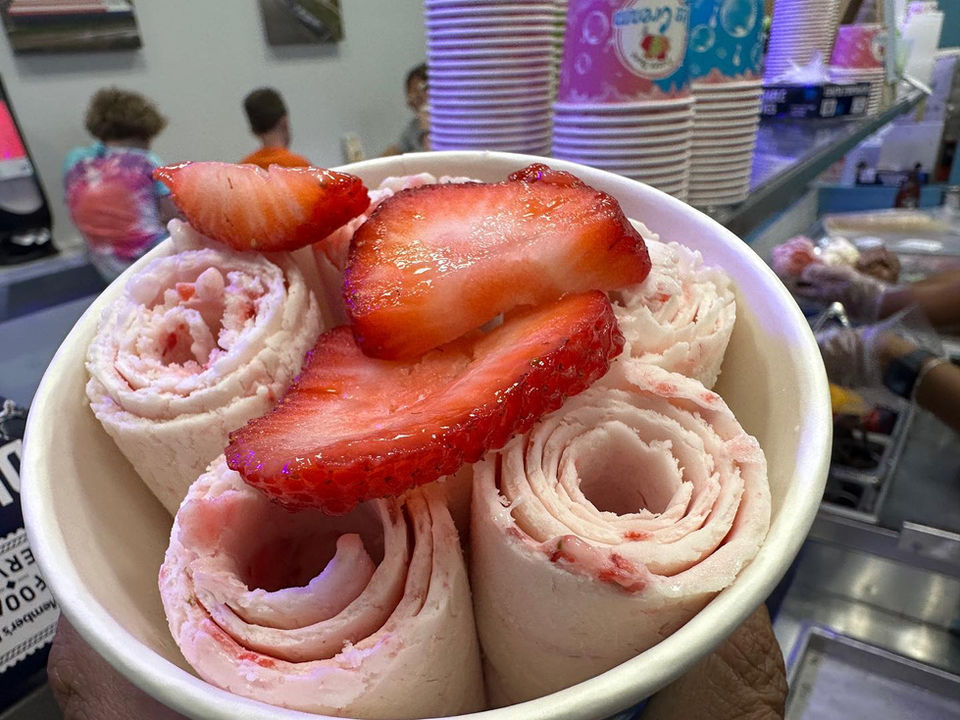 Fresh strawberry rolled ice cream in bowl with sliced strawberries.