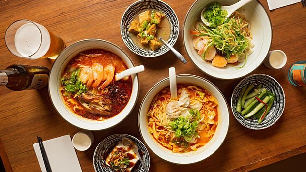 Various delicious noodle dishes and beer on a wooden table. LE SHRIMP NOODLE BAR.