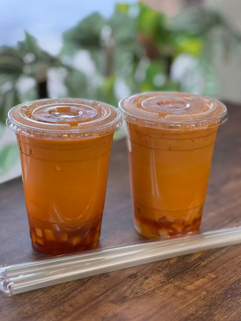 Two iced Thai tea drinks with plastic lids and straws close up.