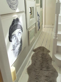 A white painted halway with gallery wall in white frames, and a grey sheepskin rug on the floor
