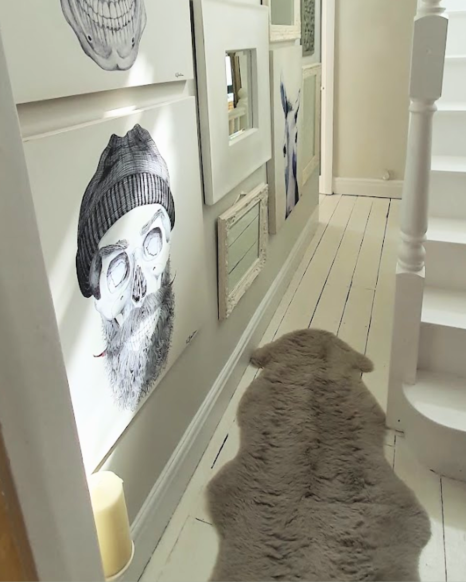 A white painted halway with gallery wall in white frames, and a grey sheepskin rug on the floor