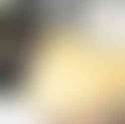 A yellow and cream textured cushion with small florals and birds, pictured on a cream boucle armchair with medium oak armrests