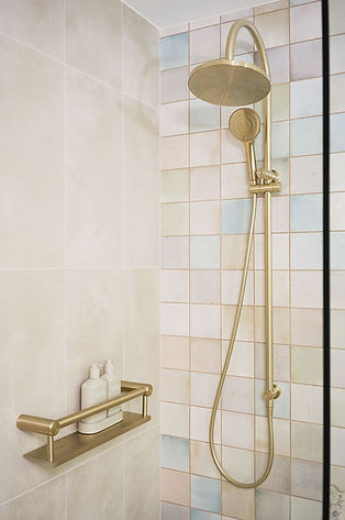 Brushed gold accessibility shower rail and grab rail with an integrated shelf, beside pastel sorbet shower tiles.