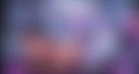 NSFW visual novel scene showing a silver-skinned oni with glowing purple markings and a horn having sex with a muscular human samurai. The oni grips the man’s hips from behind, thrusting into him. The samurai, with long black hair, braces himself on hands and knees, looking back with a mix of strain and arousal. They are set in a steamy hot spring environment, with lantern light glowing in the background. A text box at the bottom contains erotic narration.