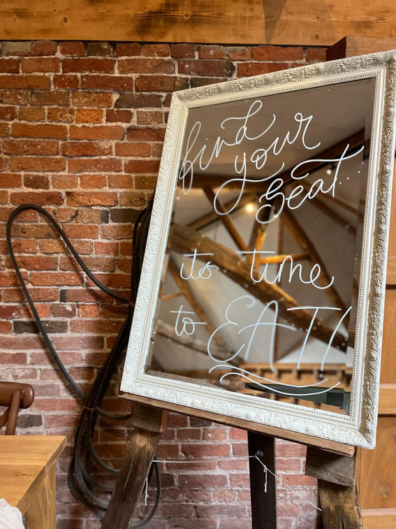 Large mirror in a wedding barn with the handwritten phrase 'find your seat its time to eat'