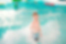 Kleiner Junge steht im Wellenbecken in den Wellen und grinst.