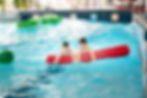 Zwei Jungen halten sich an einer Schwimmnudel fest und treiben im Wellenbecken.