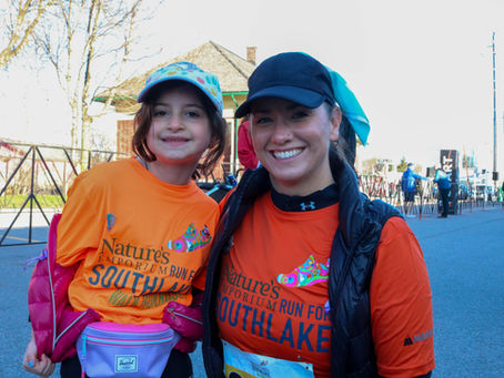 A woman and young girl smile at the camera in their orange Nature’s Emporium Run for Southlake shirts at the 2025 event.