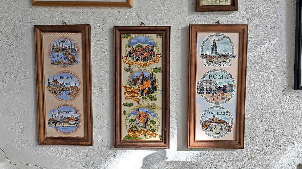 Three framed illustrations on a textured wall depict landmarks of London, Prague, Venice, Alexandria, Rome, and Carthage with vivid colors.