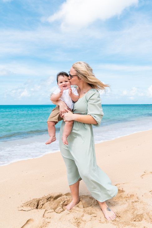 Mother kissing her baby's cheek as she stands on the beach.