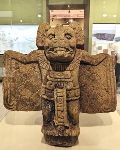 Ancient stone guardian statue with bat-like wings displayed in a museum gallery.