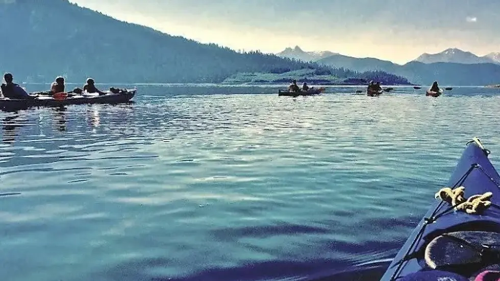 Kayakers glide across a serene lake, surrounded by majestic mountains under a clear sky.