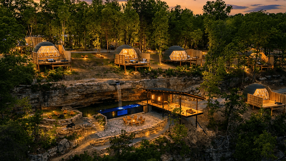 Dome-shaped glamping units nestled among trees, overlook a serene landscape complete with a waterfall and a cozy communal fire area at The Glamping Collective.