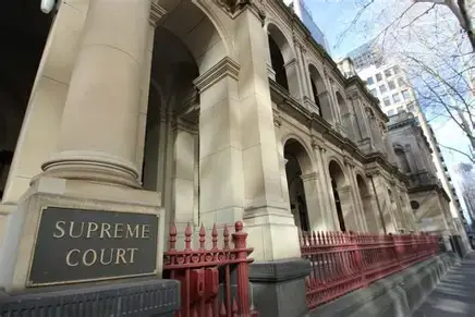 Supreme Court of Victoria building exterior with stone arches, red iron fence, and a Supreme Court sign on the left side of the walkway.