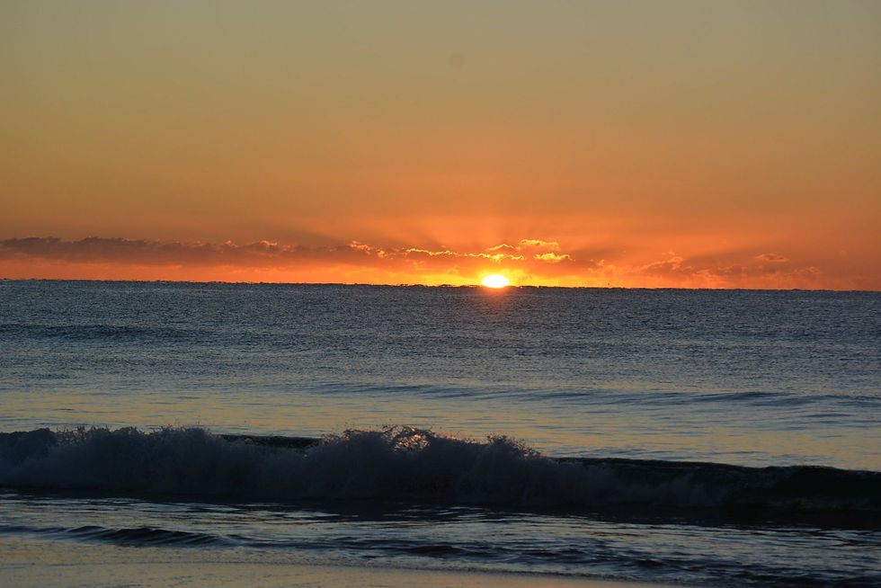 Sunset over the ocean with orange sky, glowing sun on the horizon, and dark waves in the foreground.