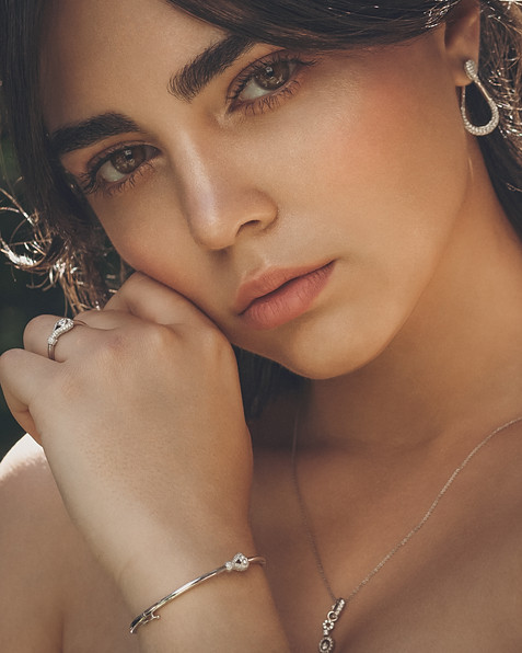 Portrait of a women with hand next to her face wearing silver diamond earrings necklace ring and bracelet