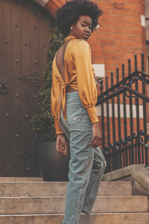 African American women with yellow silky top and blue jeans standing on a staircase looking over her shoulder