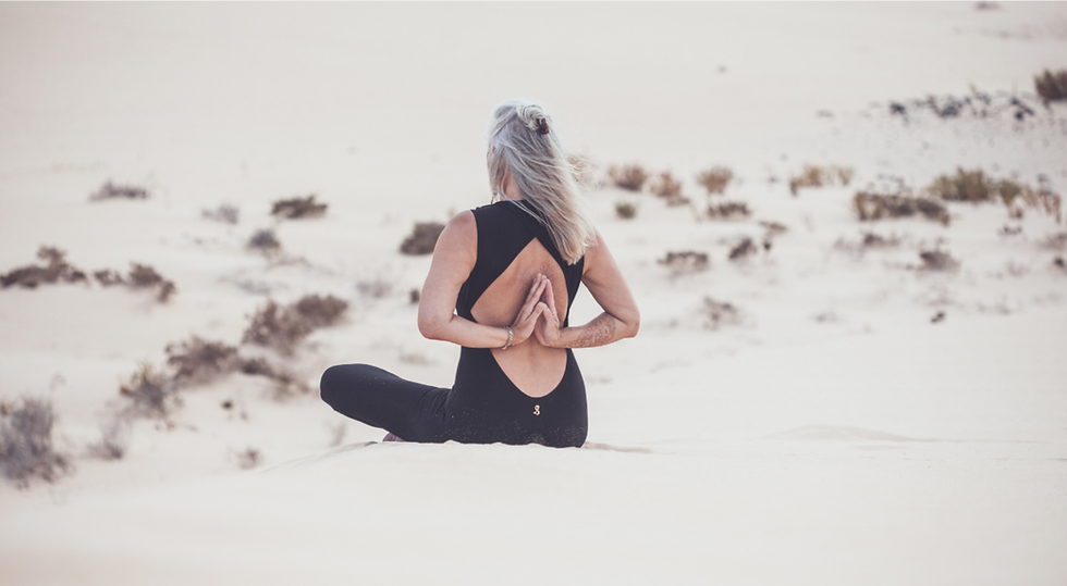 Yogini-Ela sitzt meditativ auf einer Sanddüne - Yoga bedeutet mehr als Bewegung und Entspannung