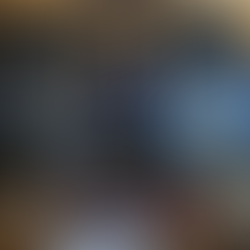 Ornate bedroom interior at Ajuda Palace featuring a dark wooden canopy bed draped with rich gold and blue fabrics. The room’s walls are covered in blue and gold patterned wallpaper, complementing the regal textiles. Flanked by two matching cabinets, the bed anchors the space, which also includes a carved wooden chair and a large decorative bowl in the foreground. Framed portraits and gilded accents throughout reinforce the room’s historic, royal ambiance.