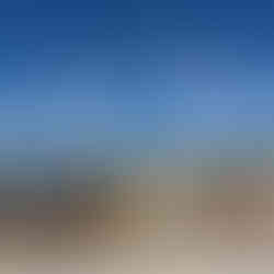 Panoramic view from the terrace of Lisbon’s National Pantheon, overlooking a sunlit cityscape of red-tiled rooftops and historic buildings. In the distance, the Tagus River stretches across the horizon, with the far shoreline visible under a clear blue sky. The vantage point captures the architectural charm and coastal beauty of Lisbon from above.