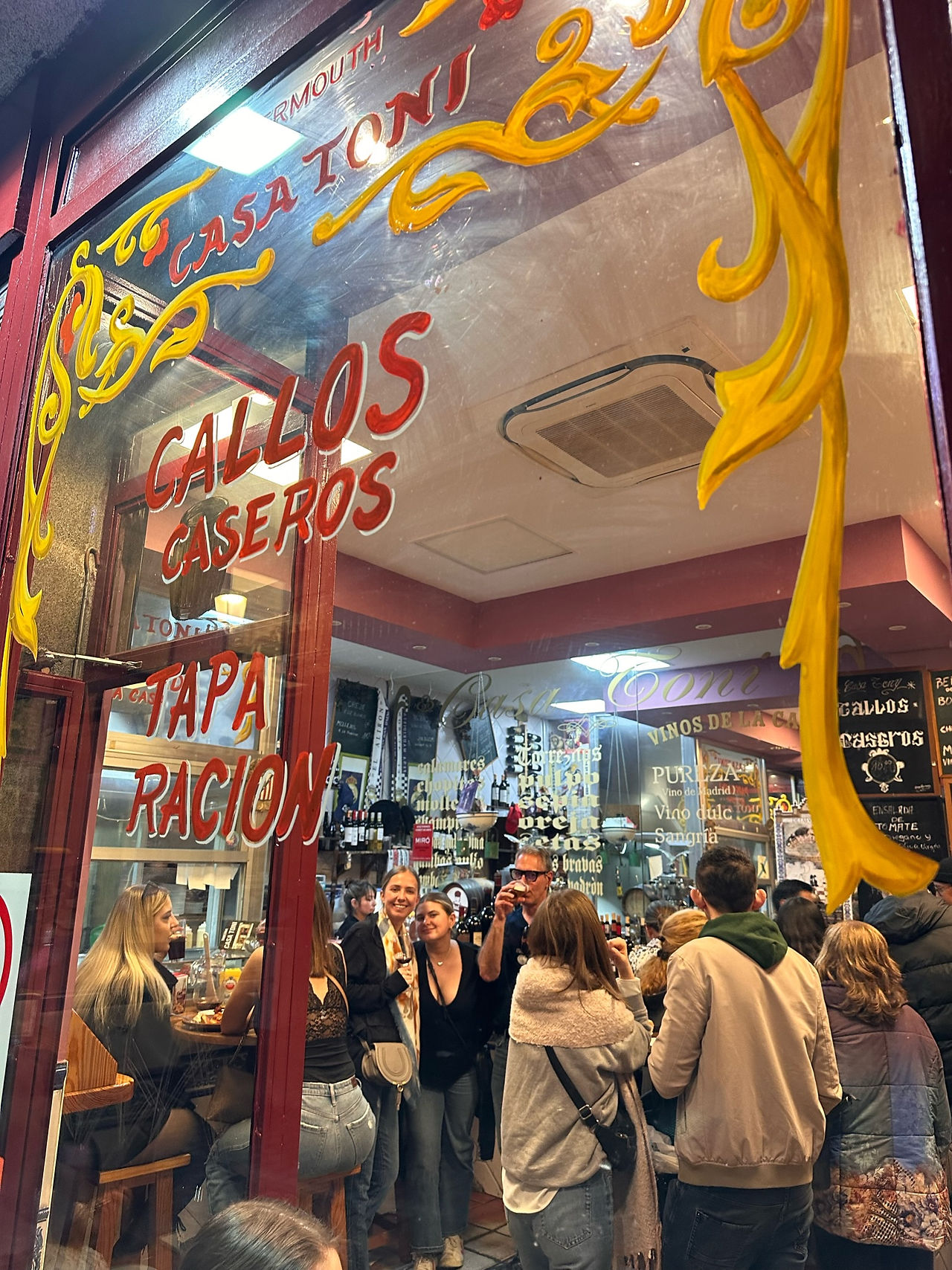 The illuminated storefront of Casa Toni in Madrid, with a crowd gathered outside at night.