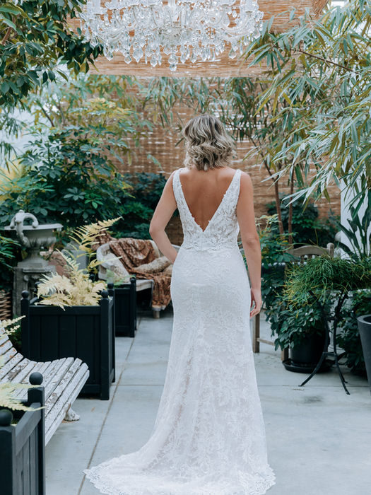 Bruid van achteren gezien in een kanten jurk met een open rug op een terras.