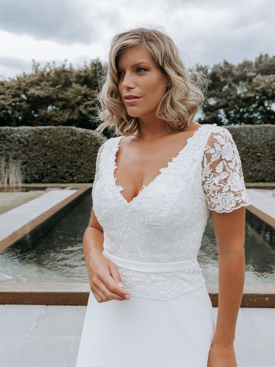 Bruidsmodel in elegante jurk bij zwembad met waterval — Divine Curves collectie Youniek Bruidsmode Turnhout