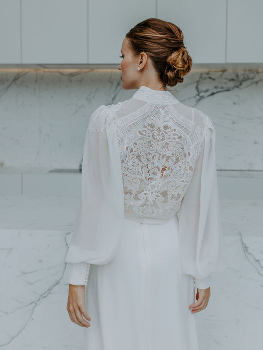 Detail van de achterzijde van een kanten bruidsoutfit met een knoopsluiting en lange mouwen.