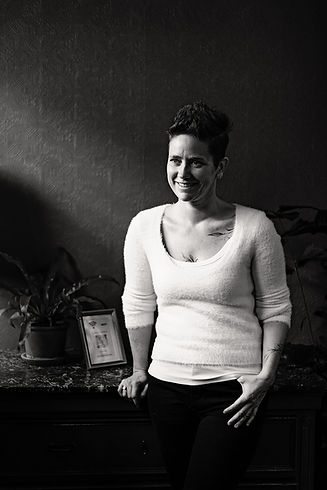 Caroline Nijs Photography wearing white sweater agains dark wall, photo by Kati Photography and Film Zürich