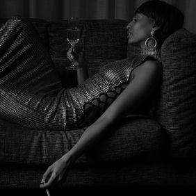 woman in profile, reclining with a drink on a velvet couch. Mood is contemplative, unposed.